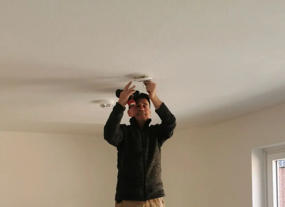 An installer on a step ladder working overhead at a ceiling fixture opening in an empty room